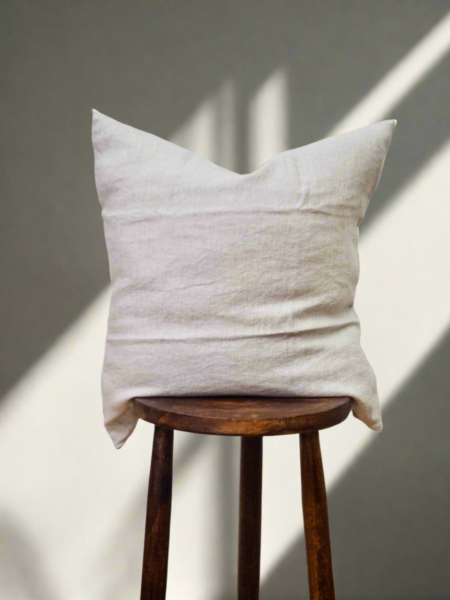 Linen Cushion Cover in Oatmeal - TSL| placed on a stool with soft lighting 