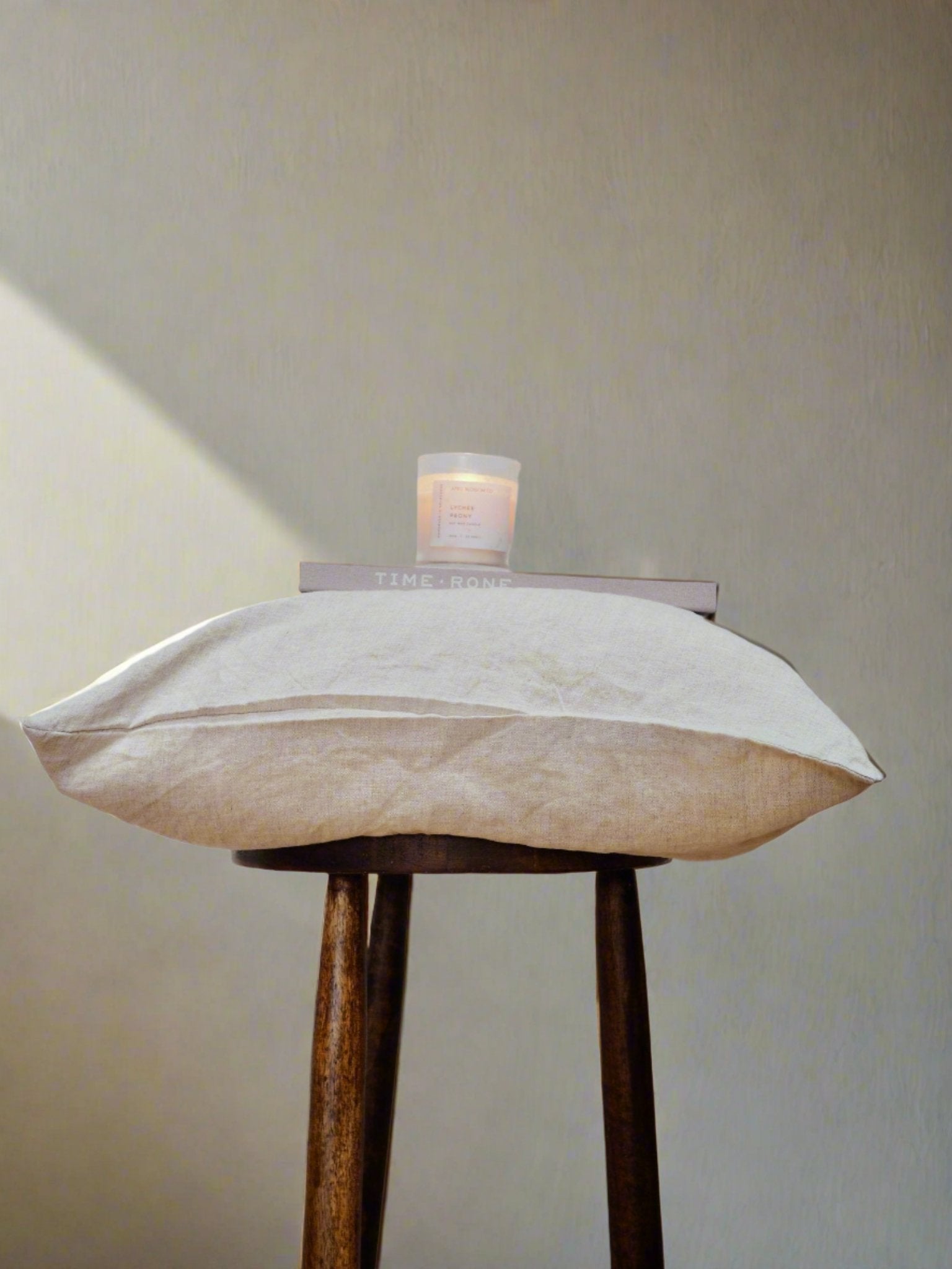 Linen Cushion Cover in Oatmeal - TSL| throw pillow placed on a stool with decor pieces such as book and candle on top 
