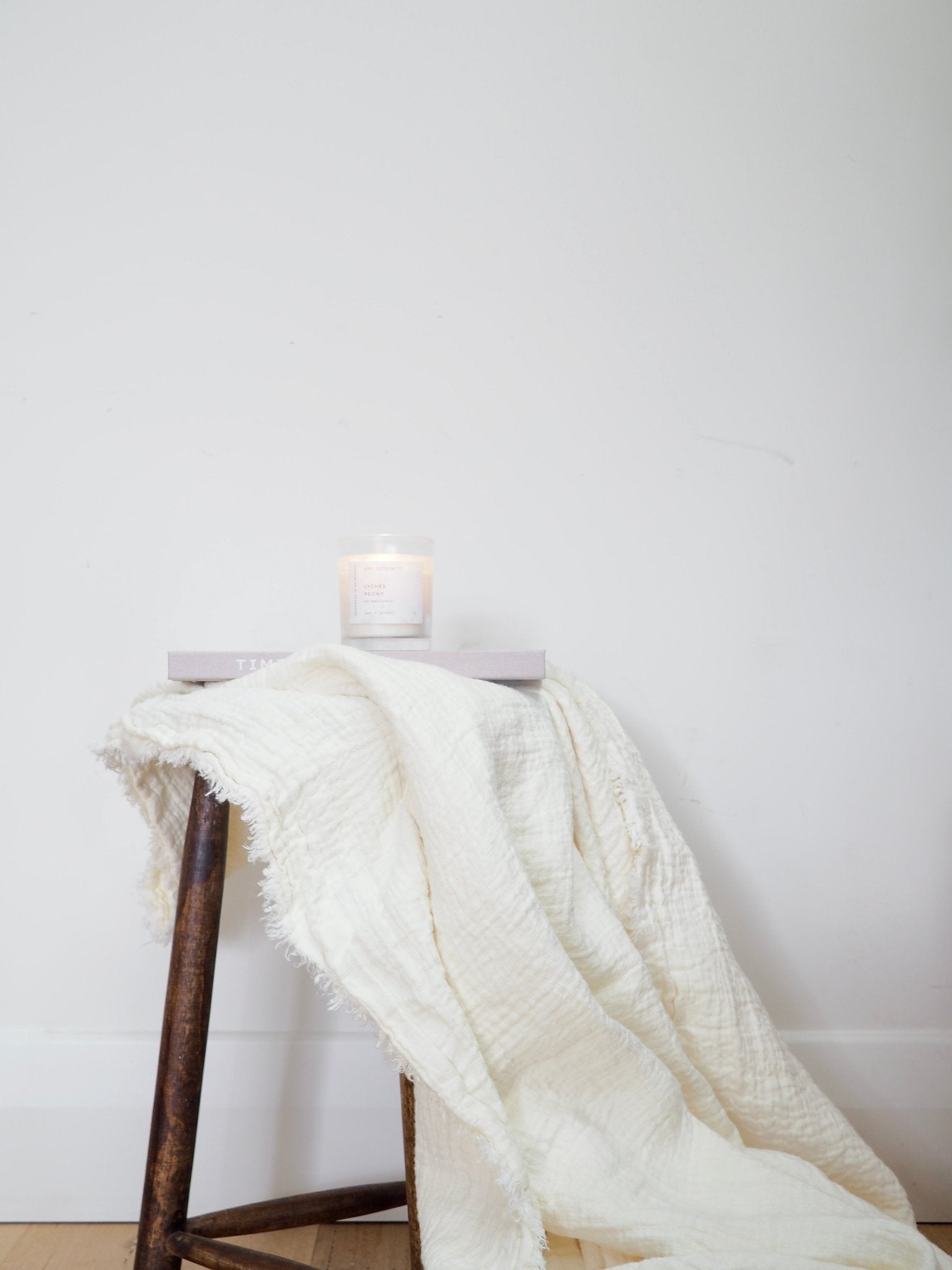 Pure linen throw blanket in white draped on a rustic stool to show  fringed detailing.