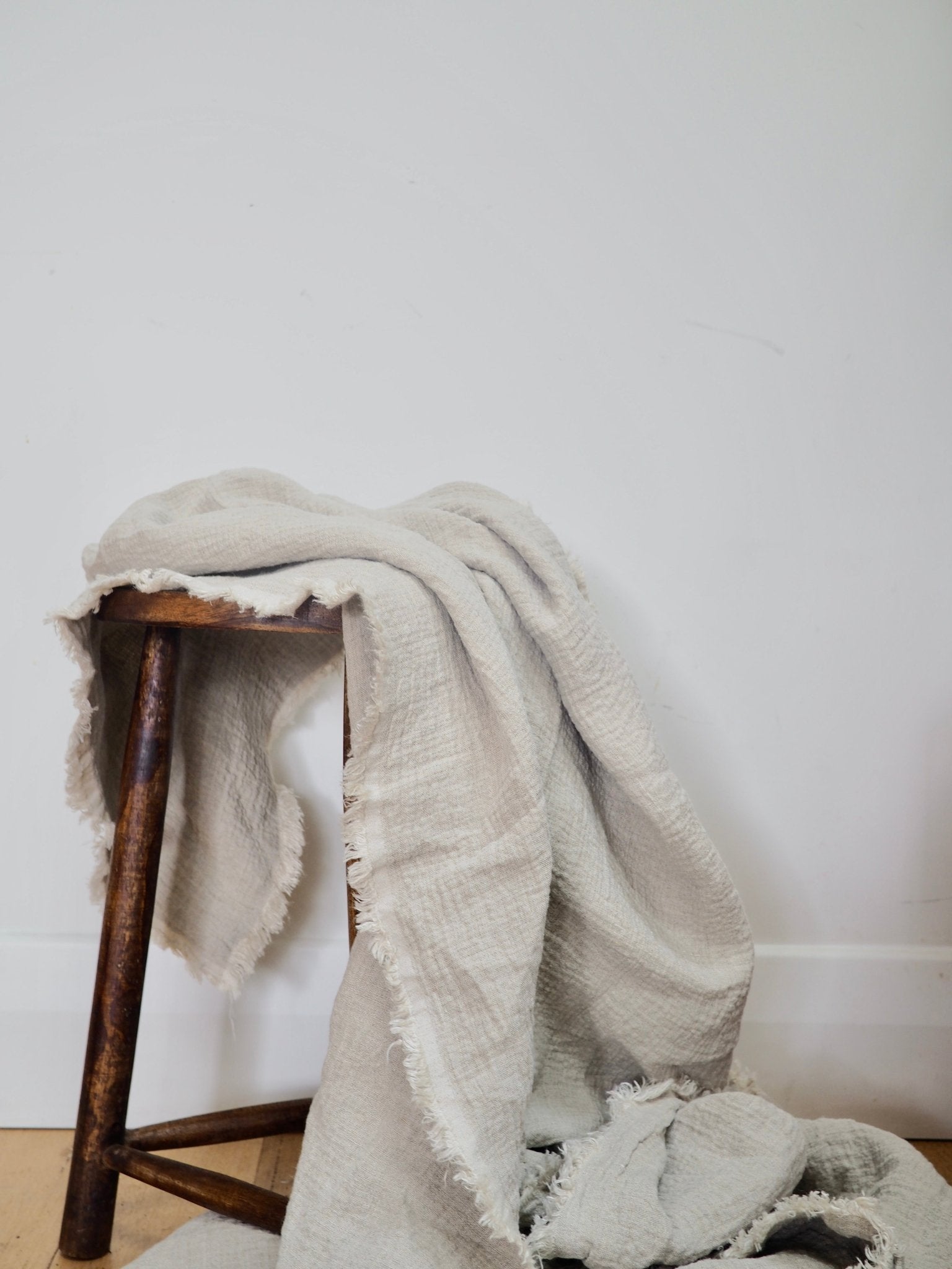 Heavyweight linen blanket in natural colour flowing from a rustic stool to show its large length and fringed detailing.